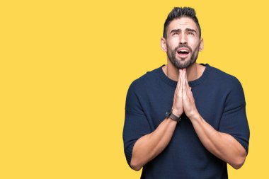 Yalvarıyor ve umut ifade yüzünde çok duygusal ve endişe ile birlikte elleriyle dua izole arka plan üzerinde kazak giyen genç yakışıklı adam. Bağışlanmak. Din kavramı.