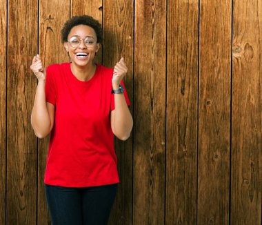 Güzel genç Afro-Amerikan kadın izole arka plan üzerinde kutluyor gözlük takan şaşırttı ve silah ile başarı için yükseltilmiş ve açık gözler hayrete düşürdü. Kazanan kavramı.