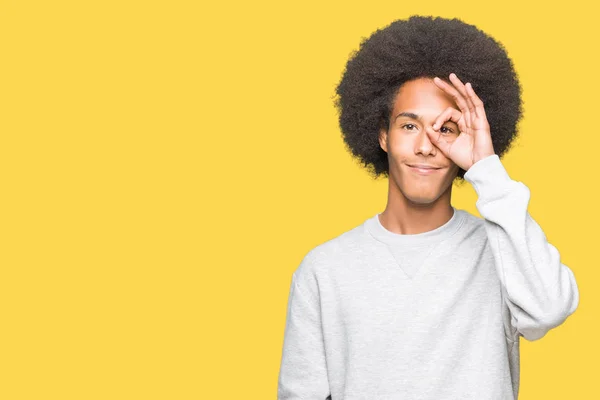 年轻的非洲裔美国男子与非洲裔头发穿着运动运动衫做Ok手势与手微笑 眼睛透过手指看快乐的脸 — 图库照片