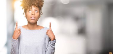 İzole arka plan güzel genç Afro-Amerikan kadın hayrete ve yukarıya bakıyor ve parmakları ile işaret ve silah kaldırdı şaşırttı.