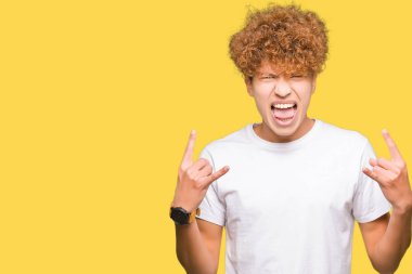 Afro saç ile genç yakışıklı adam rahat beyaz t-shirt deli ifade ile eller yukarı kaya sembolü yapıyor bağırarak giyiyor. Müzik yıldızı. Ağır kavram.