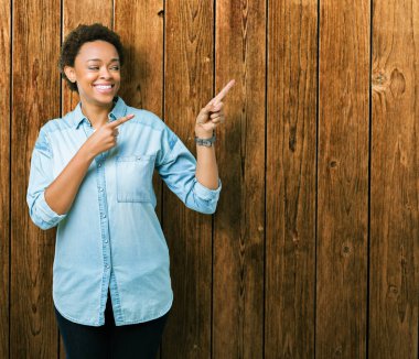 Gülümseyen ve iki elleri ve parmakları ile tarafına işaret kamera bakarak izole arka plan üzerinde genç güzel bir Afrikalı-Amerikalı kadın.