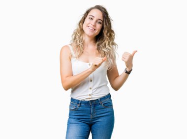 İzole arka plan üzerinde sarışın güzel genç kadın kendine güvenen gülümseyerek arkasından el ve başparmak yukarıya, işaret