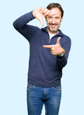 Orta yaş yakışıklı adam mutlu yüzü ile elleri ve parmakları ile çerçeve yapma gülümseyen bir kazak giyiyor. Yaratıcılık ve fotoğrafçılık konsepti.