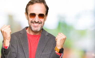 Orta yaş yakışıklı iş adamı kutluyor güneş gözlüğü takıyor şaşırttı ve silah ile başarı için yükseltilmiş ve açık gözler hayrete düşürdü. Kazanan kavramı.