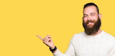 Yüzünde, kocaman bir gülümseme ile kış kazak giyen genç hipster adam kameraya bakarak yan el ve parmak ile işaret.