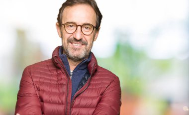 Orta yaş yakışıklı adamın gözlük ve kış ceket ile mutlu yüz gülümseyen giydiğini silah kameraya bakarak geçti. Olumlu bir kişi.