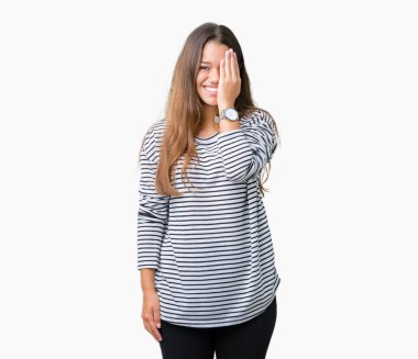 El yüz ve sürpriz duygu kendinden emin gülümseme ile tek gözüyle kapsayan izole arka plan üzerinde çizgili süveter giyen genç güzel esmer kadın.