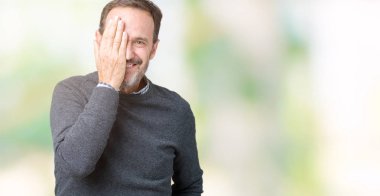 Yakışıklı orta yaş komuta sizde bir göz ile yüz ve sürpriz duygu kendinden emin gülümseme ile el kapsayan izole arka plan üzerinde bir kazak giyiyor.