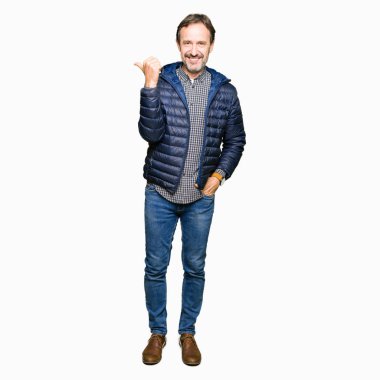 Orta yaş yakışıklı adam kış ceket giyiyor mutlu yüz görünümlü ve başparmak yukarı ile yan işaret gülümseyen.