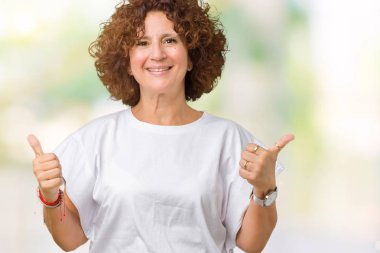 El ile pozitif jest yapıyor izole arka plan başarı işareti üzerinde beyaz t-shirt giyen kadın güzel orta ager kıdemli başparmak gülümseyen ve mutlu. Neşeli bir ifadeyle, kazanan jest kameraya bakıyor.