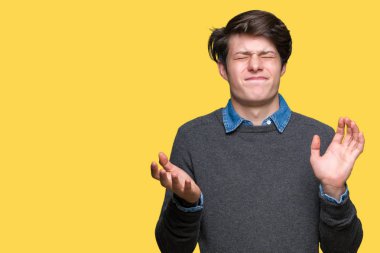 Izole arka plan üzerinde genç yakışıklı zarif adam silah ve elleri kaldırdı ile anlamsız ve karışık ifade. Şüphe kavramı.