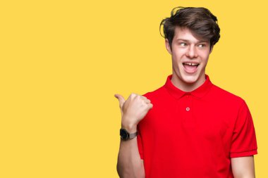 Izole arka plan üzerinde kırmızı t-shirt giyen genç yakışıklı adam mutlu yüz görünümlü gülümseyerek ve başparmak ile yan işaret.