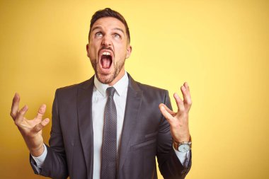 Genç yakışıklı iş adamı sarı arka planda çılgın ve kızgın bir şekilde bağırıyor ve agresif bir ifade ve kolla bağırıyor. Hayal kırıklığı konsepti.