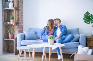 Genç güzel çift oturan ve çevrelerinde karton kutular ile yeni dairede kanepede sarılma, çok yeni bir eve taşımak için heyecanlı