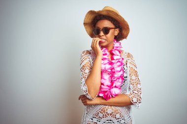 Afro saçlı genç afro-amerikan kadın izole arka plan üzerinde çiçek hawaiian lei giyen stresli ve ağız tırnak ısırma elleri ile sinir görünümlü. Anksiyete sorunu.