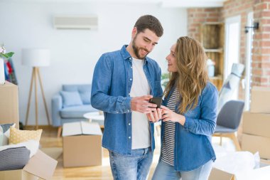 Genç çift karton kutular etrafında akıllı telefon kullanarak yeni bir eve hareket