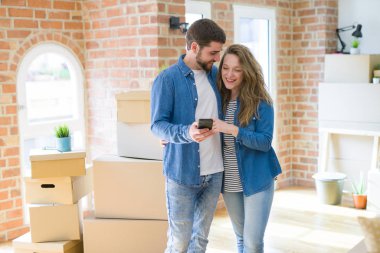 Genç çift karton kutular etrafında akıllı telefon kullanarak yeni bir eve hareket