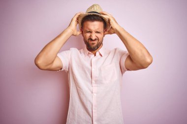 Yakışıklı adam pembe izole arka plan üzerinde şapka ve yazlık gömlek giyen baş ağrısı umutsuz muzdarip ve stresli çünkü ağrı ve migren. Eller baş üstünde.