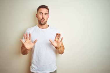 İzole edilmiş arka plan üzerine gündelik beyaz tişört giyen genç yakışıklı. Avuçlarını kaldırıyor, reddediyor ve iğrenç bir ifadeyle reddediyor. Dur ve yasakla.