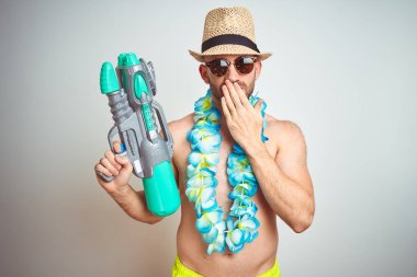 Yaz şapkası ve Hawaii çiçekleri takan genç adam su tabancasını izole edilmiş arka planda tutuyordu. Ağzını kapatıyordu. Yanlışlıktan dolayı utancı, korkunun ifadesi, sessizlikten korkması, gizli bir konsept.