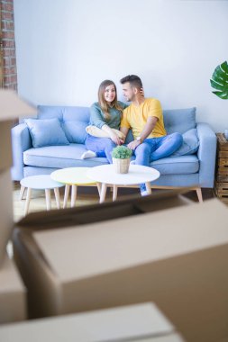 Genç güzel çift oturan ve çevrelerinde karton kutular ile yeni dairede kanepede sarılma, çok yeni bir eve taşımak için heyecanlı