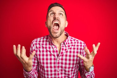 Genç ve yakışıklı bir adam arka planda izole edilmiş çılgın ve kızgın bir şekilde bağırıyor ve agresif bir ifade ve kolla bağırıyor. Hayal kırıklığı konsepti.
