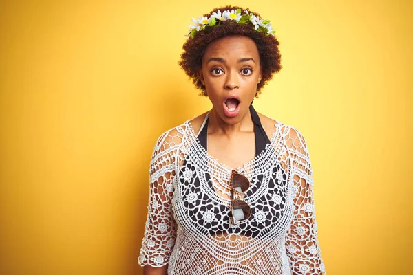 Young african american woman with afro hair wearing flowers crown over yellow isolated background afraid and shocked with surprise expression, fear and excited face.