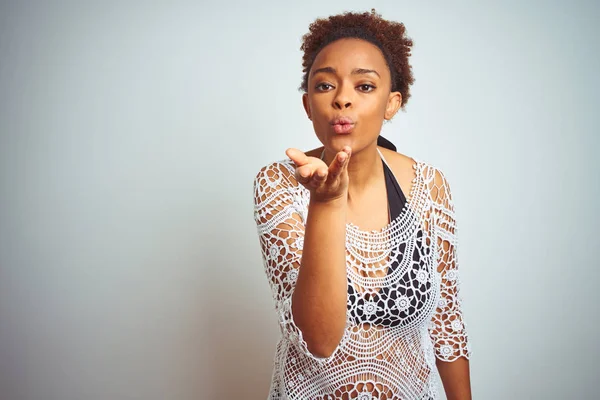 Young african american woman with afro hair wearing a bikini over white isolated background looking at the camera blowing a kiss with hand on air being lovely and sexy. Love expression.