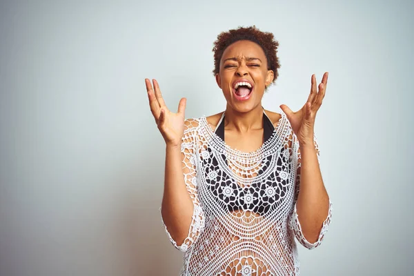 Young african american woman with afro hair wearing a bikini over white isolated background celebrating mad and crazy for success with arms raised and closed eyes screaming excited. Winner concept