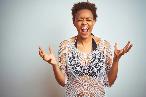 Young african american woman with afro hair wearing a bikini over white isolated background crazy and mad shouting and yelling with aggressive expression and arms raised. Frustration concept.