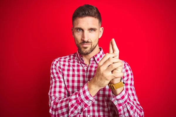 Young handsome man over red isolated background Holding symbolic gun with hand gesture, playing killing shooting weapons, angry face