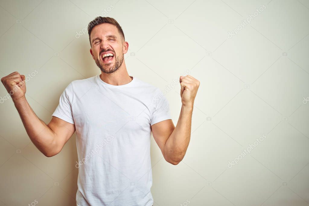 Young handsome man wearing casual white t-shirt over isolated background celebrating surprised and amazed for success with arms raised and eyes closed. Winner concept.
