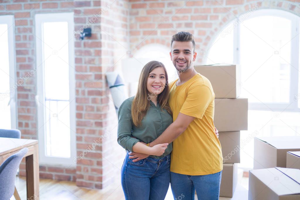 Young beautiful couple in love around cardboard boxes moving to new home, smiling very happy and cheerful for new apartment