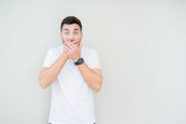 Üzerinde rahat beyaz t-shirt giyen genç yakışıklı adam arka plan ağız hata için elleriyle kapsayan şok izole. Gizli kavramı.