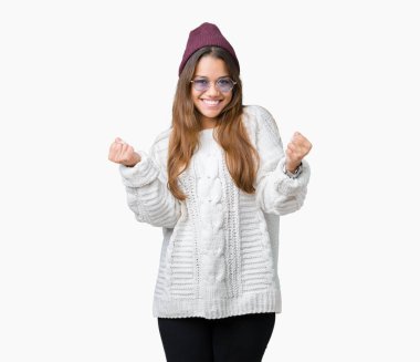 Güneş gözlüğü izole arka plan kutlama üzerinde giyen genç güzel esmer hipster kadın şaşırttı ve başarı için kaldırdı kollarını açarak hayret ve gözleri açık. Kazanan kavramı.