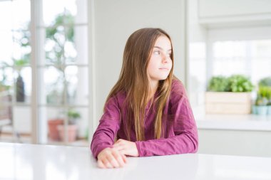 Beyaz masada güzel genç kız çocuk yan arıyor, güvenli bir gülümseme ile doğal yüz ile profil poz rahatlayın.