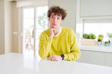 Çene düşünme hakkında soru, dalgın ifade üzerine evde el ile sarı kazak giyen genç yakışıklı adam. Düşünceli yüzüyle gülümsüyor. Şüphe kavramı.