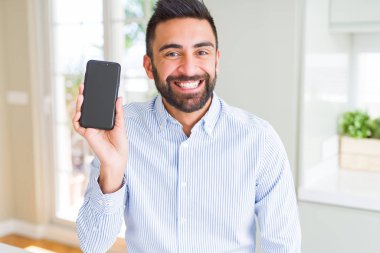 Yakışıklı İspanyol iş adamı ayakta mutlu bir yüz ile akıllı telefon ekranı gösteren ve dişleri gösteren kendinden emin bir gülümseme ile gülümseyerek