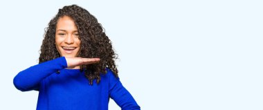 Kıvırcık saçlı Genç güzel kadın, büyük ve büyük boy işareti, ölçmek sembolü gösteren eller ile gebelik kış kazak giyiyor. Kameraya bakarak gülümsüyor. Ölçme konsepti.