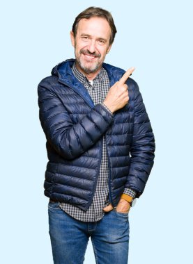 Orta yaş yakışıklı adam neşeli bir gülümseme ile el ve parmak kadar yan yüzünde mutlu ve doğal ifade ile işaret yüz ile bir kış palto giyiyor