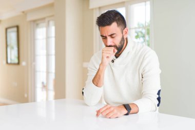 Yakışıklı İspanyol adam evde rahat beyaz kazak giyen rahatsız duygu ve soğuk veya bronşit için bir belirti olarak öksürük. Sağlık kavramı.