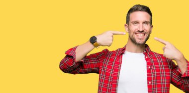 Yakışıklı adam kendinden emin gösterilen ve işaret parmakları diş ve ağız ile gülümseyen rahat gömlek giymiş. Sağlık kavramı.