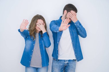 Genç güzel çift elleri ile gözleri kaplayan beyaz izole arka plan üzerinde birlikte duran ve üzgün ve korku ifade ile stop jest yapıyor. Utanmış ve olumsuz kavram.