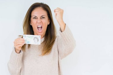 Orta yaş kadın izole arka plan üzerinde 5 £ banka notu tutan kızgın ve sinirli öfke, deli ve yükseltilmiş el, öfke kavramı ile bağırarak bağırarak