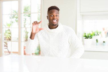 Yakışıklı afro-amerikan adam beyaz masada gülümseyen ve emin el ile el yaparken boyutu işareti parmakları ile yaparken ve kamera. Ölçü kavramı.