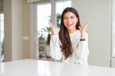 Genç güzel kadın evde beyaz masada deli ve deli kollarını kaldırdı ve kapalı gözleri heyecan çığlık ile başarı için deli kutluyor. Kazanan kavramı