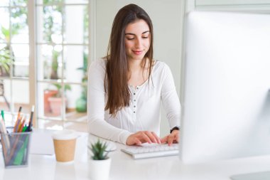 Bilgisayar kullanarak çalışan güzel genç iş kadını, gülümseyen ve online çalışma üzerinde konsantre