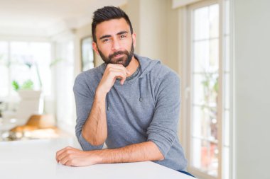 Yakışıklı İspanyol adam evde rahat sweatshirt giyen çeneüzerinde soru, dalgın ifade düşünme el iyle. Düşünceli bir yüzle gülümsüyor. Şüphe kavramı.