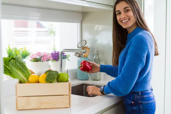 Young woman washing vegetables and fruit using water from sink